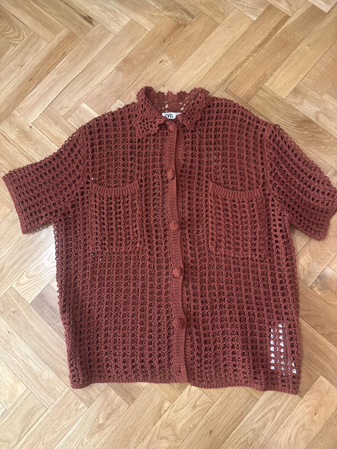 Brown open-knit shirt with buttons and two front pockets on a light wooden floor. Visible label with text "ZARA".