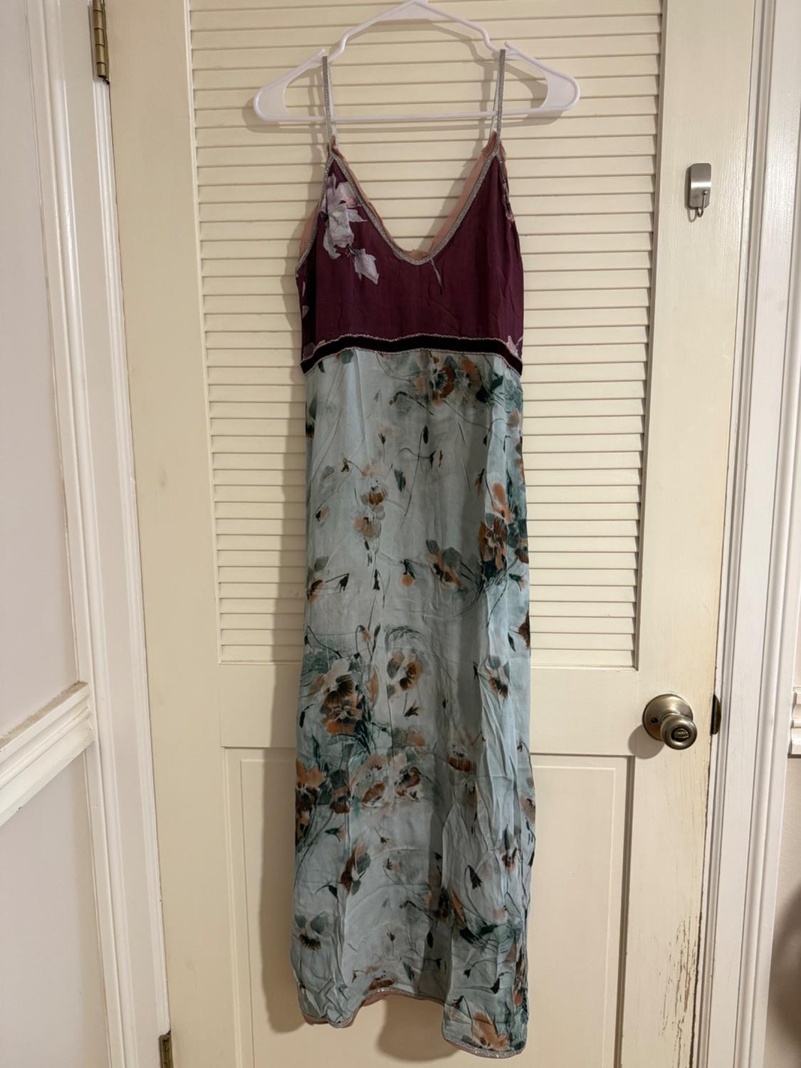 Long dress hanging on a door, with thin straps, purple top and blue skirt with floral print.