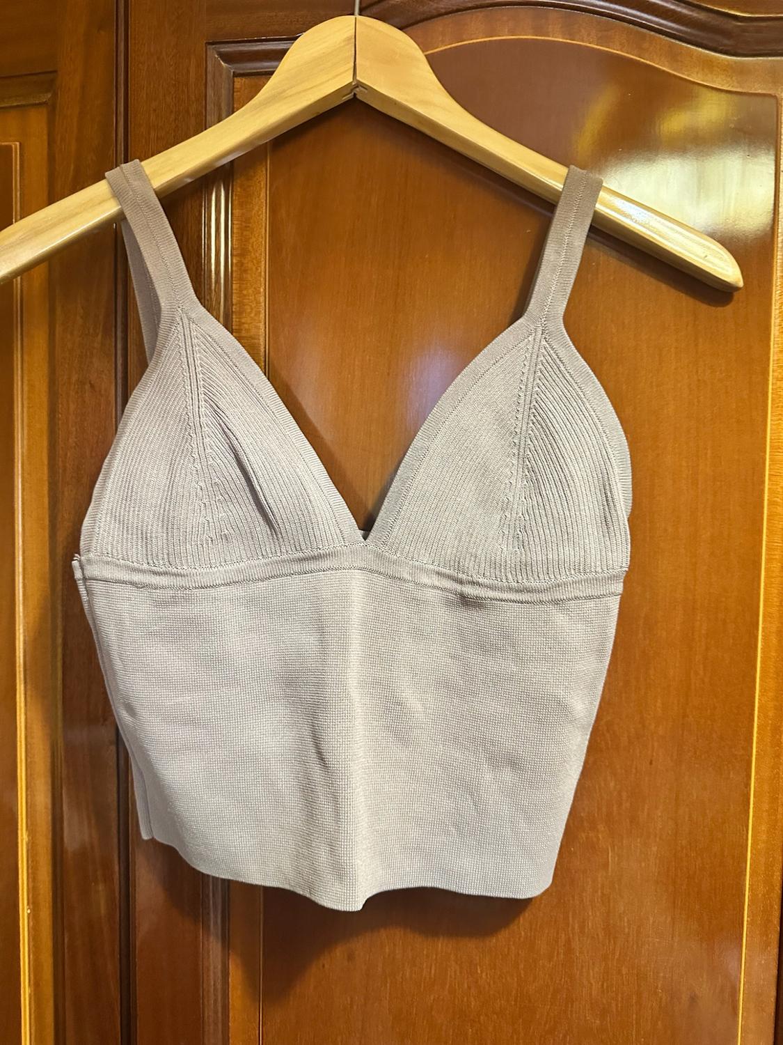Light grey ribbed knit crop top with a V-neck, hanging on a wooden hanger in front of a door.