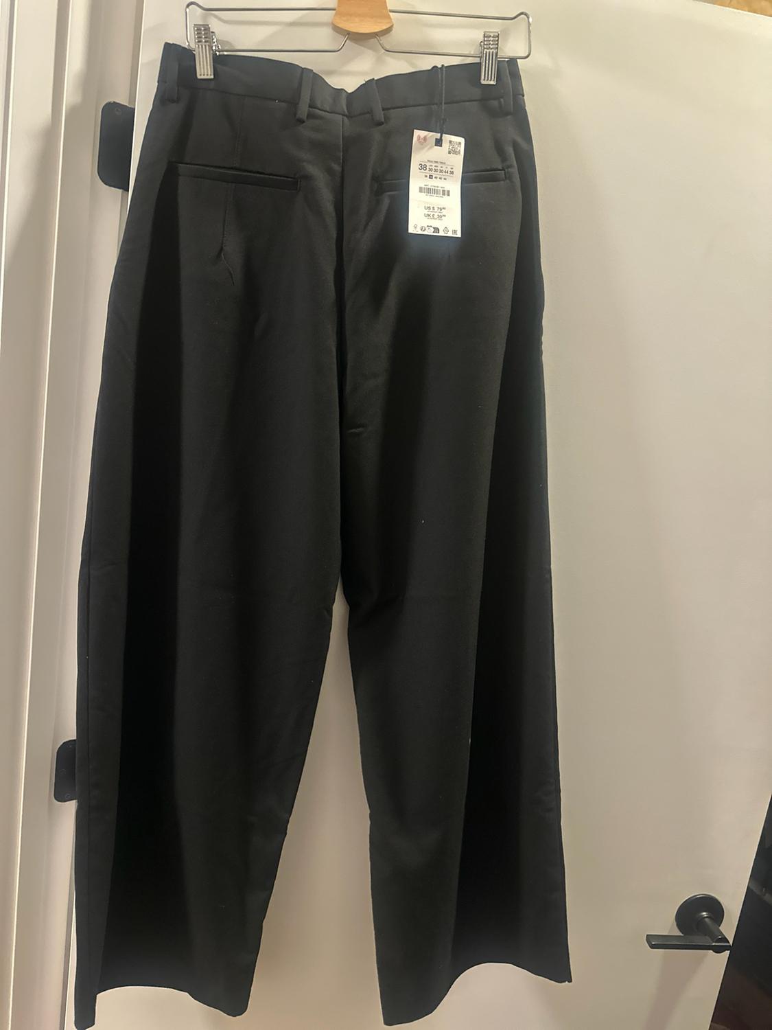 Black dress pants hanging on a hanger on a white door. Back view with pockets and a tag with the text 38.