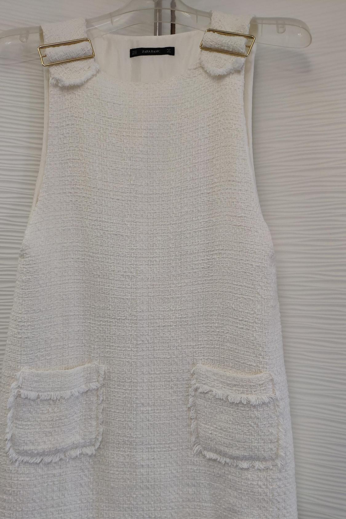 Detail of white dress with front pockets and gold buckles on the straps.
