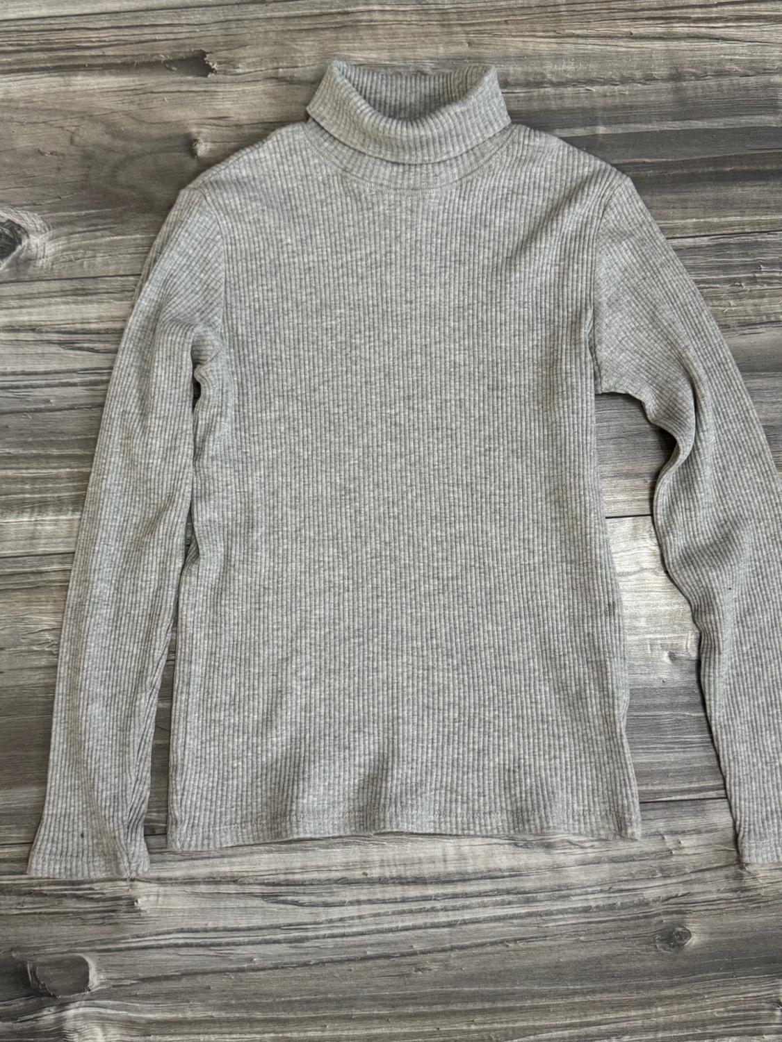 Light grey ribbed jumper with a high neck and long sleeves, placed against a rustic wooden background.