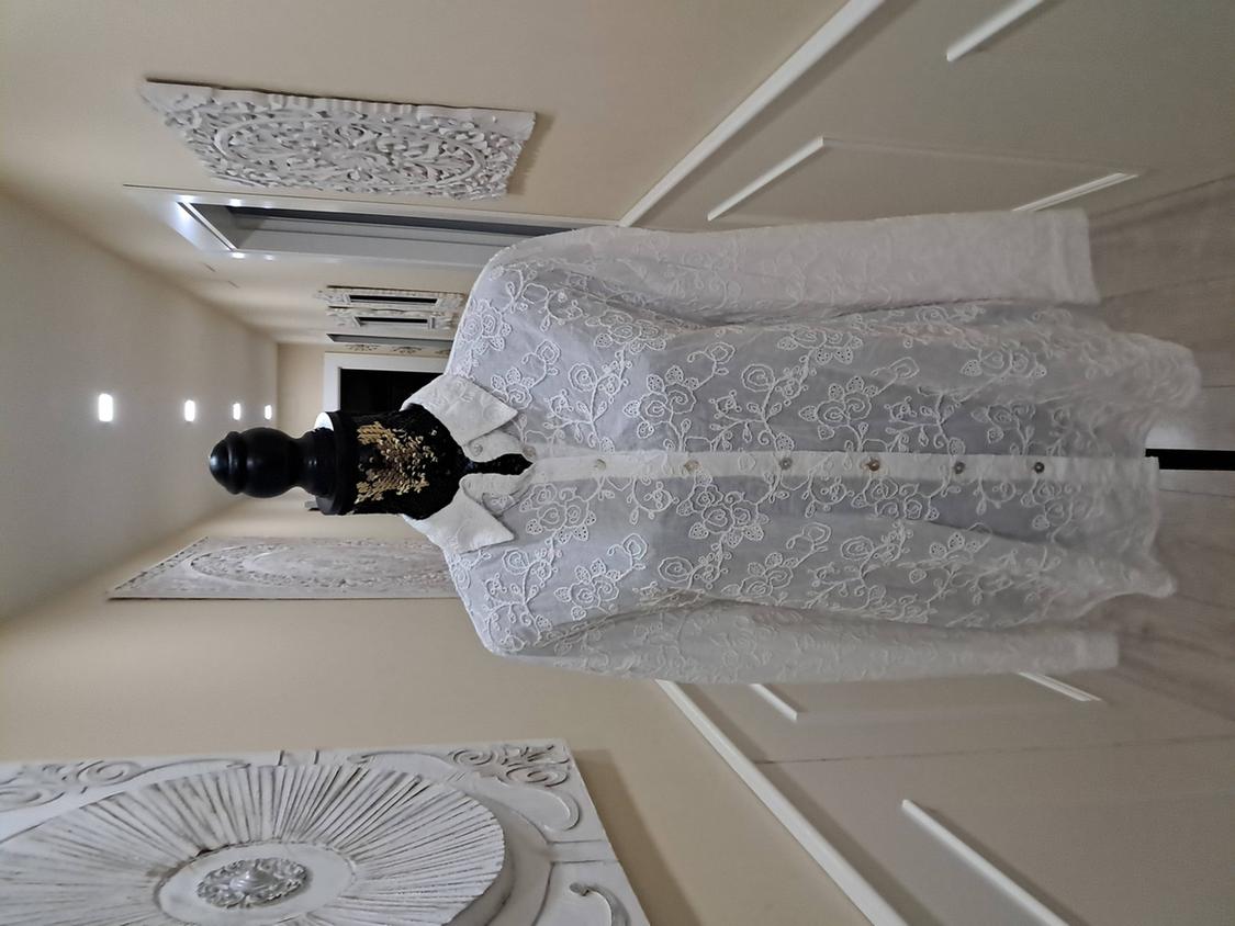 Mannequin in a white floral lace blouse in a lit hallway. Embossed wall decorations in the background.
