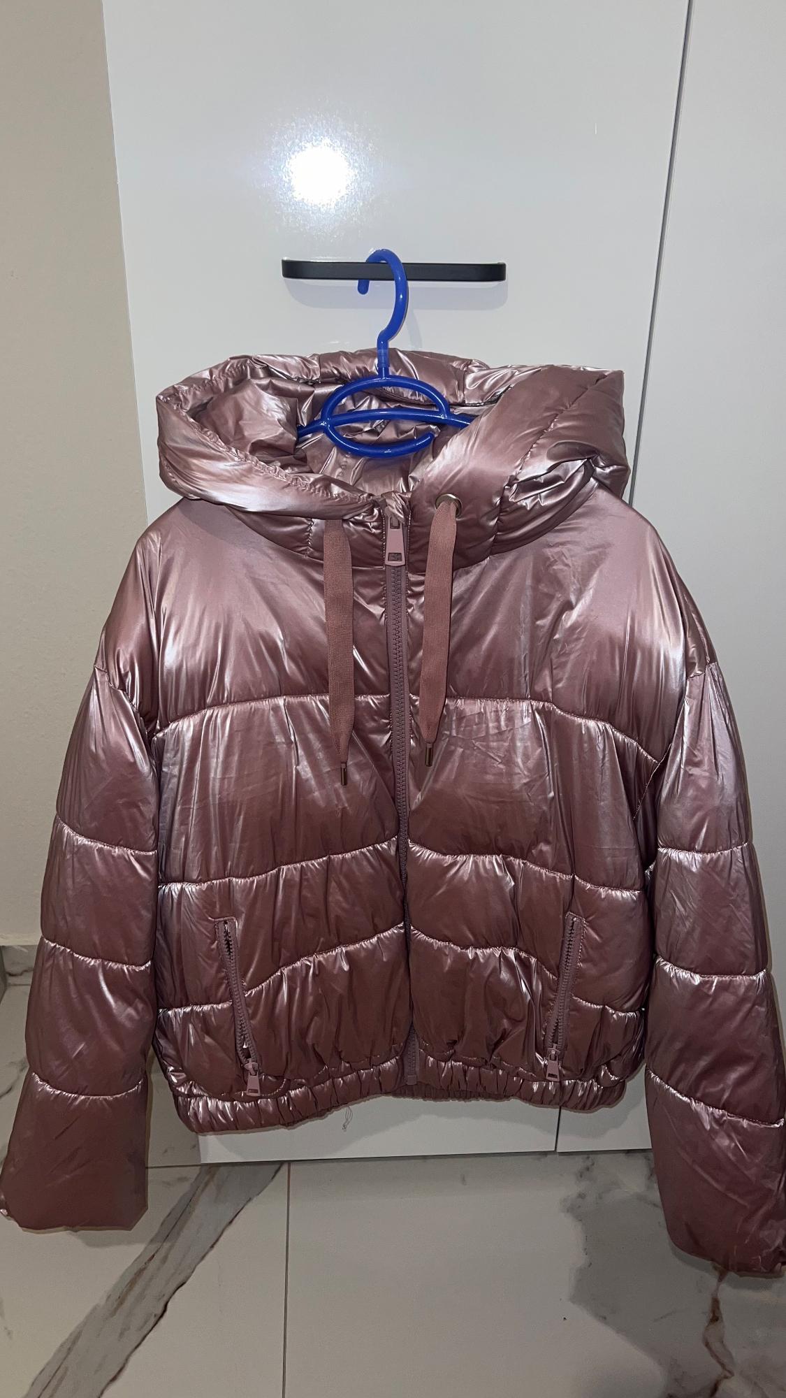 Metallic pink padded jacket hanging on a blue hanger, with a hood and drawstrings, on a bright white background.