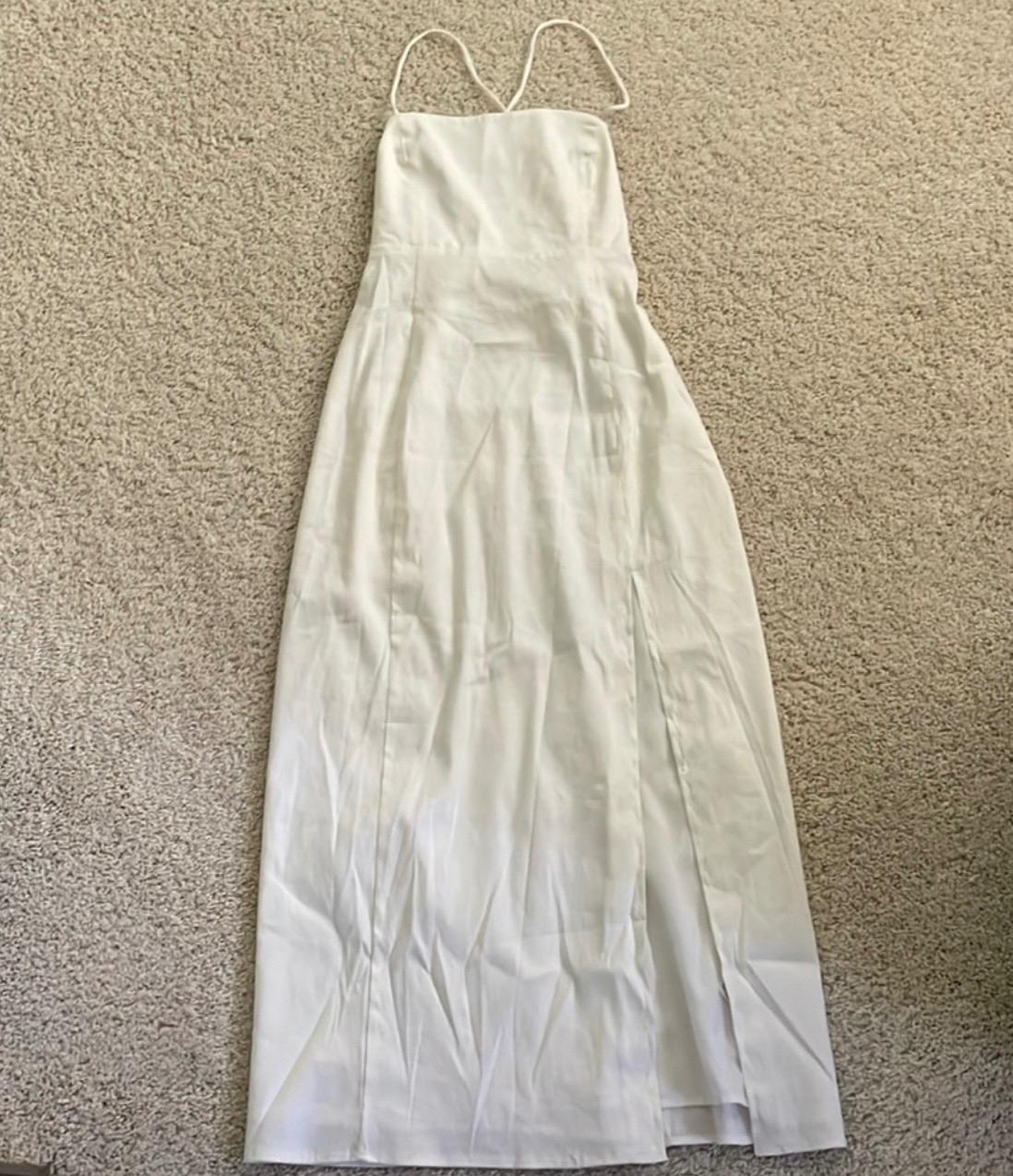 White long dress with thin straps on a beige rug. Simple and elegant design, ideal for formal occasions.