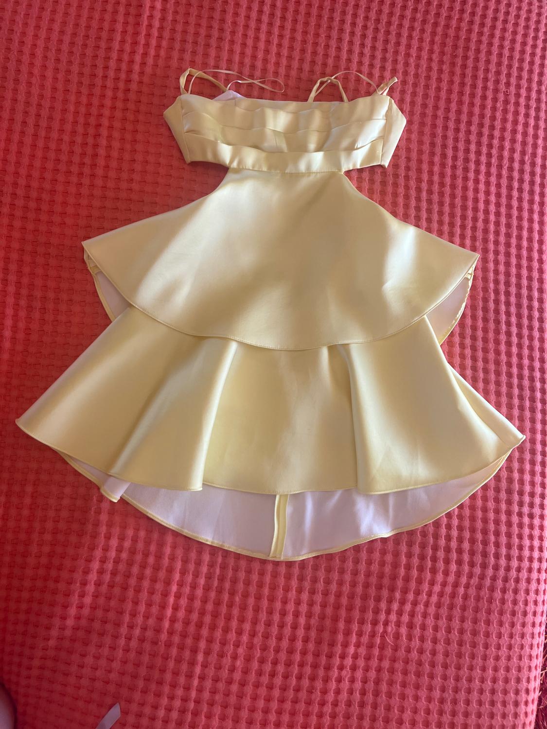 Satin yellow dress with spaghetti straps, waist cut-outs, and a ruffled skirt, against a pink fabric background.