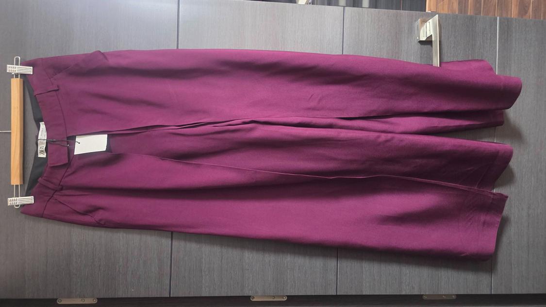 Wide-leg purple trousers hanging on a wooden hanger against a dark grey door. Label with the text ZARA.