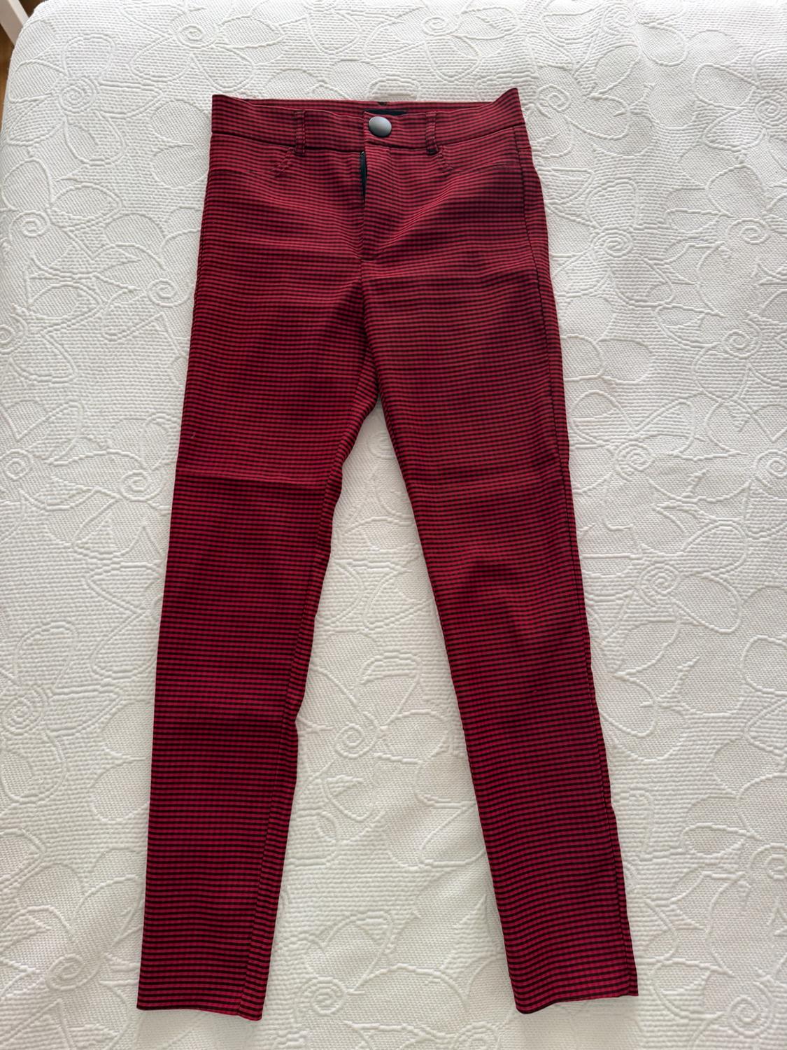 Red and black small checked trousers on a textured white bedspread. Casual, relaxed-style composition.