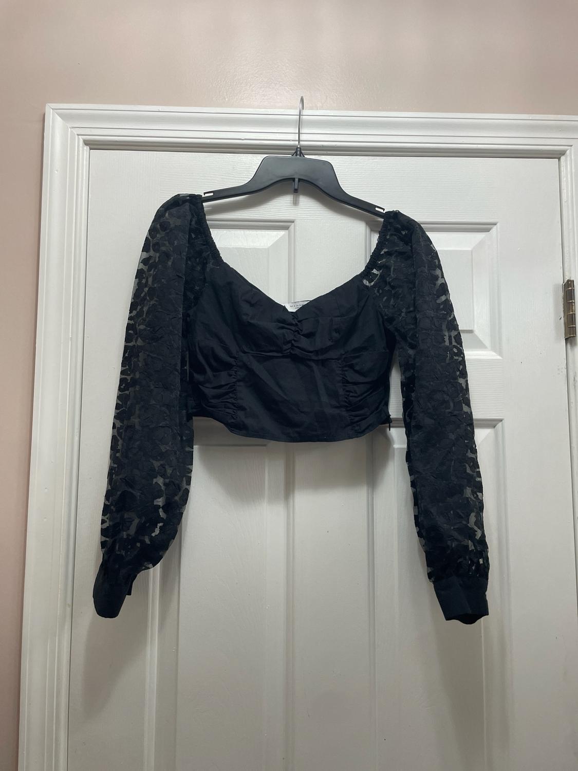 Black ruched crop top with a sweetheart neckline and long semi-sheer lace sleeves, hanging on a white door.