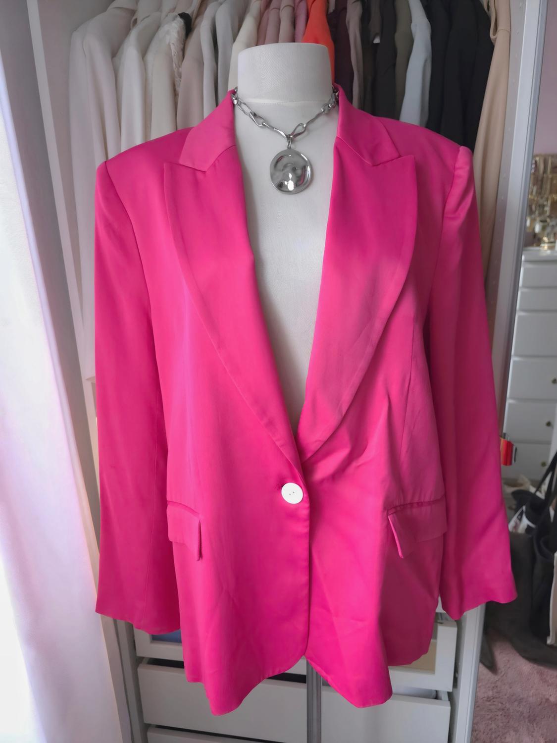 Μανεκέν με φούξια blazer και ασημένιο κολιέ. Ντουλάπα με κρεμασμένα ρούχα σε ανοιχτούς και σκούρους τόνους.