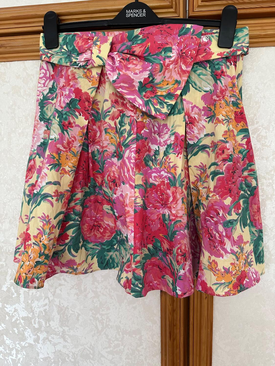 Front view of floral skirt with bow, pink, green and yellow colours, visible pleats.