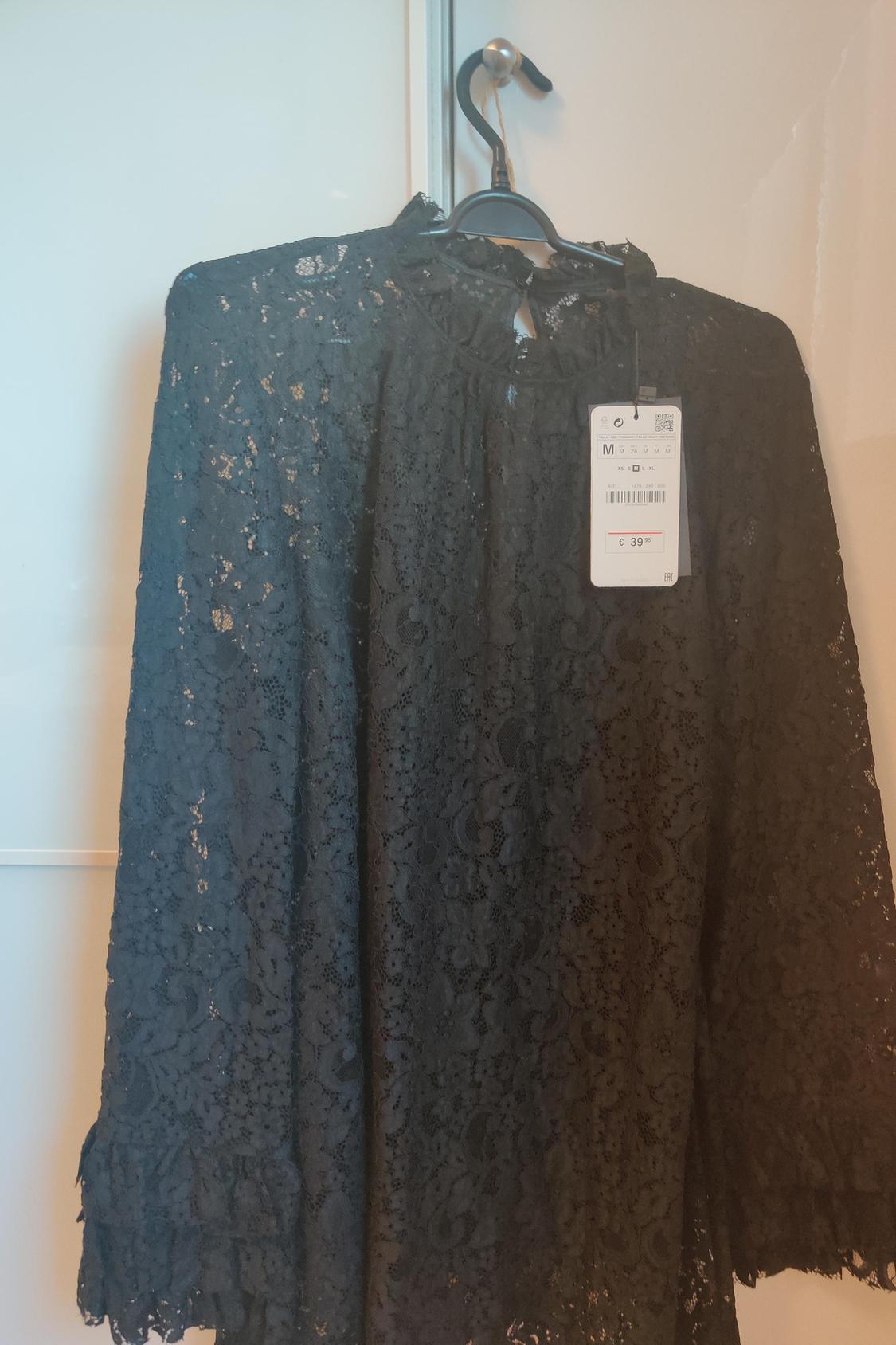 Front view of black lace blouse with visible label hanging on a hanger.