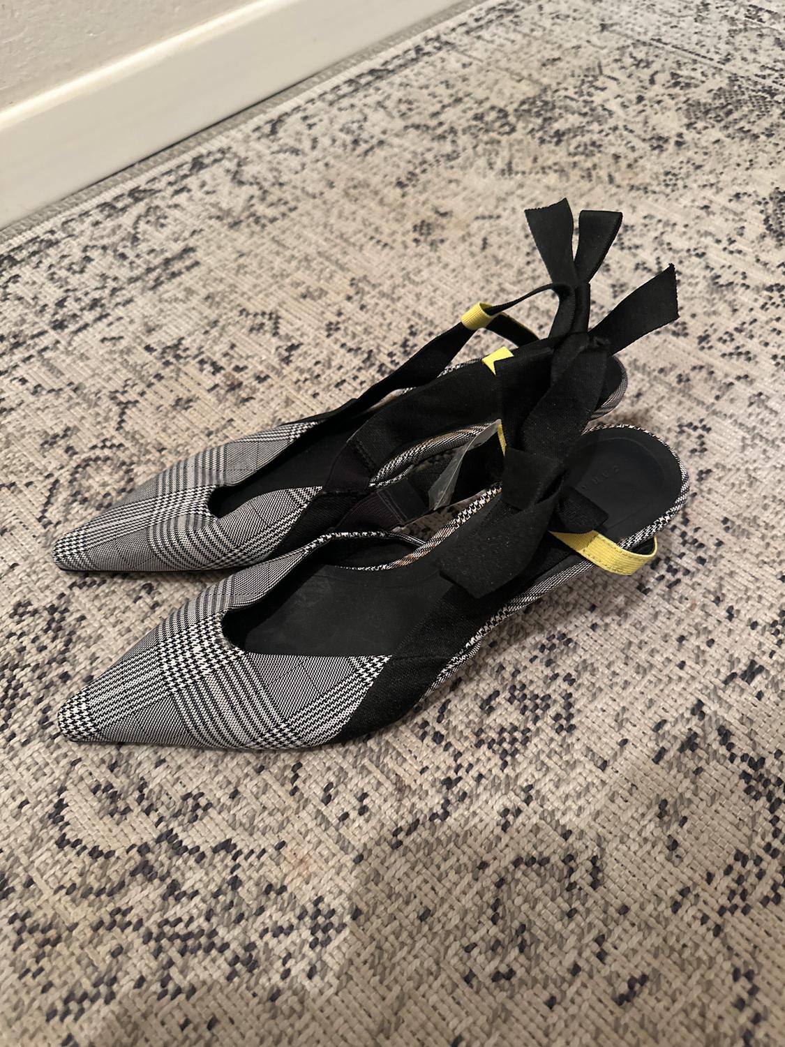 Black and white checked high heels with black ribbons and yellow detailing, on a textured rug.