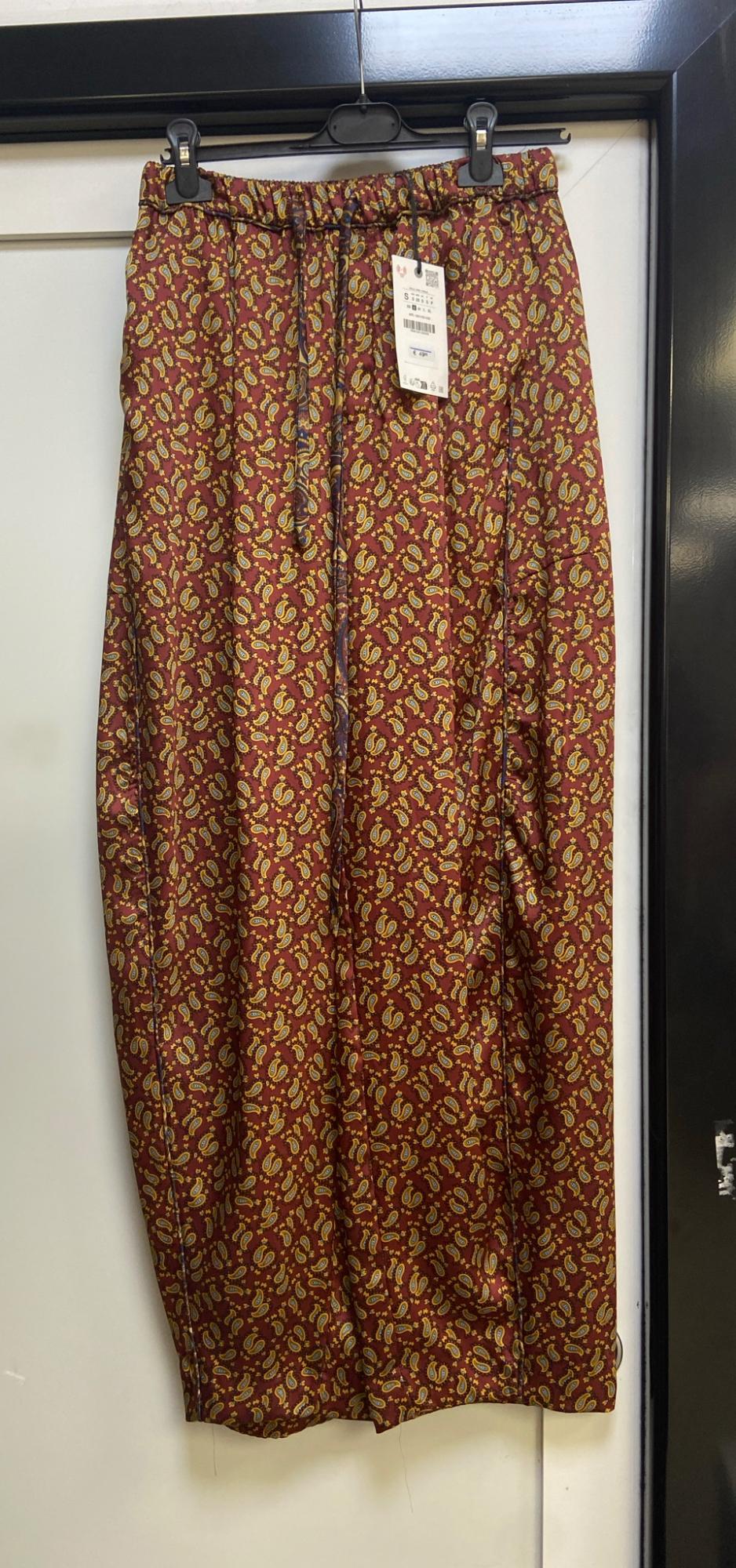 Maroon trousers with a paisley pattern, elasticated waist and drawstring, hanging on a clothes hanger against a white background.