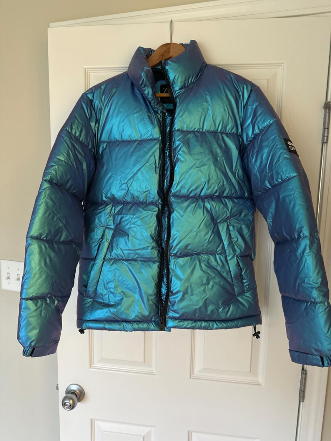 Front view of an iridescent blue padded jacket with a front zip and side pockets.