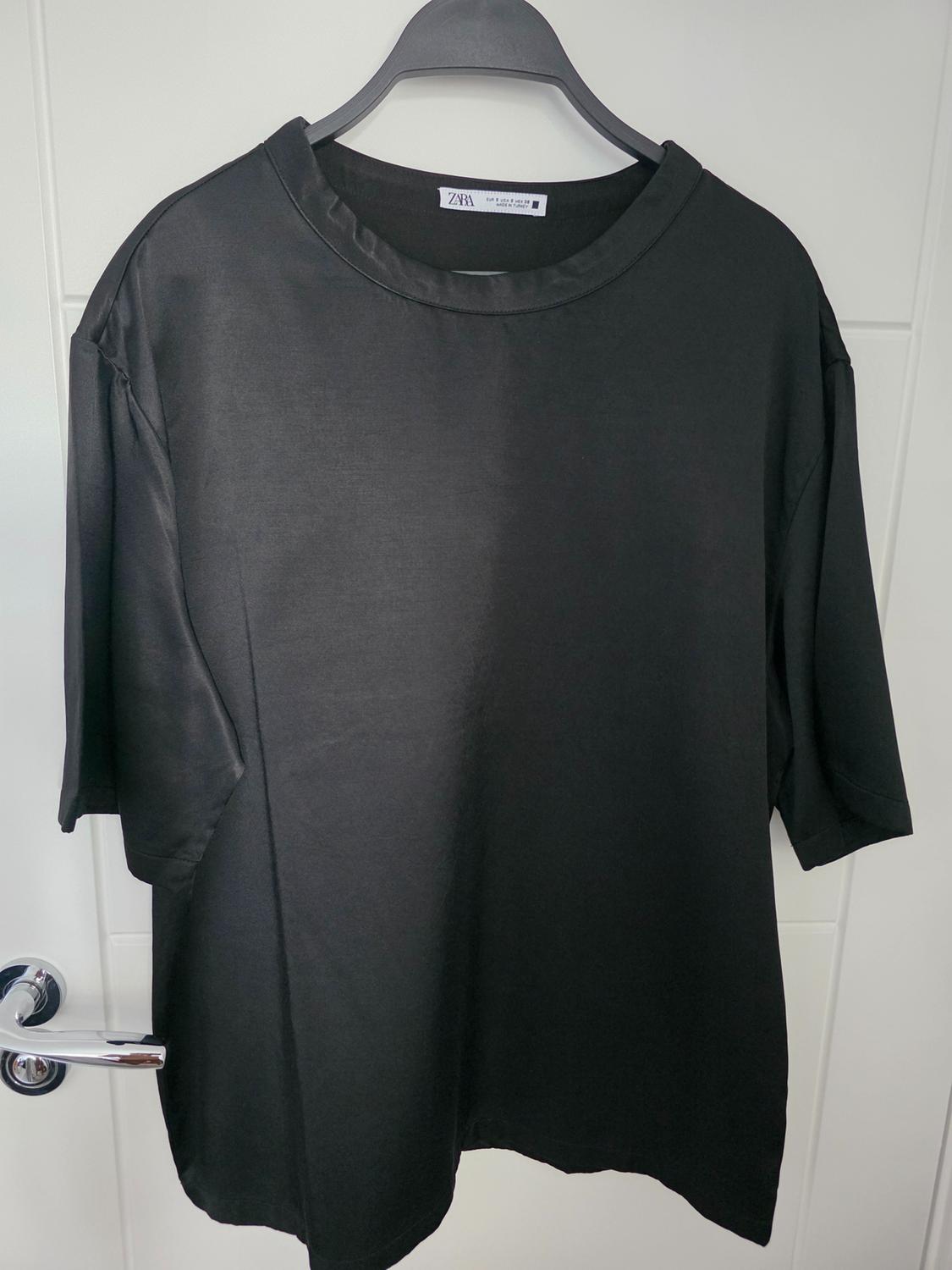 Black short-sleeved t-shirt hanging on a black hanger. Visible label with text "Zara" on the collar. White background.
