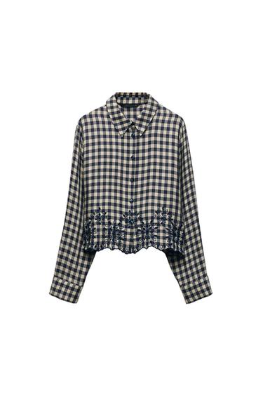Front view of a checked blouse with floral embroidery on the hem and button front.