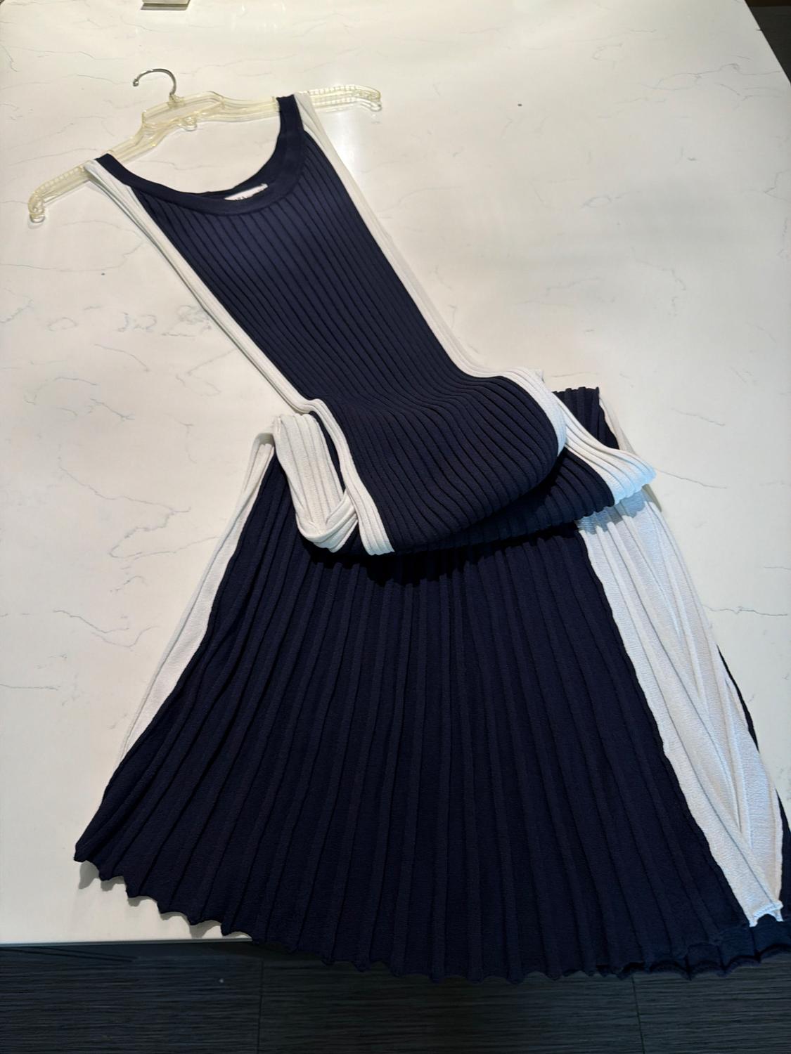 Navy and white sleeveless ribbed dress, on a transparent hanger, folded over itself on a light marble surface.