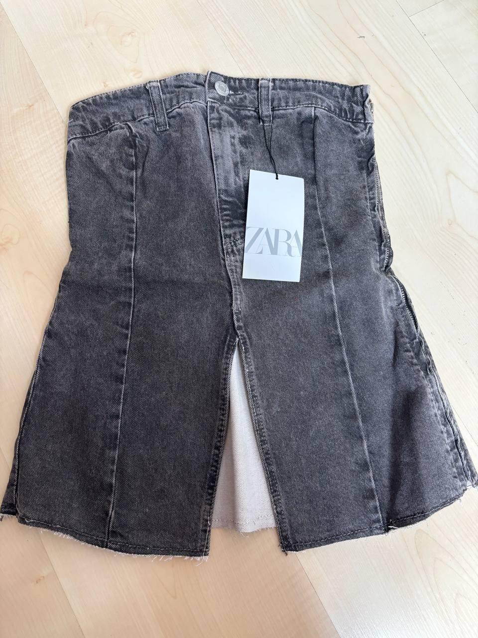 Grey denim skirt with 'ZARA' swing tag, on a light wooden floor.