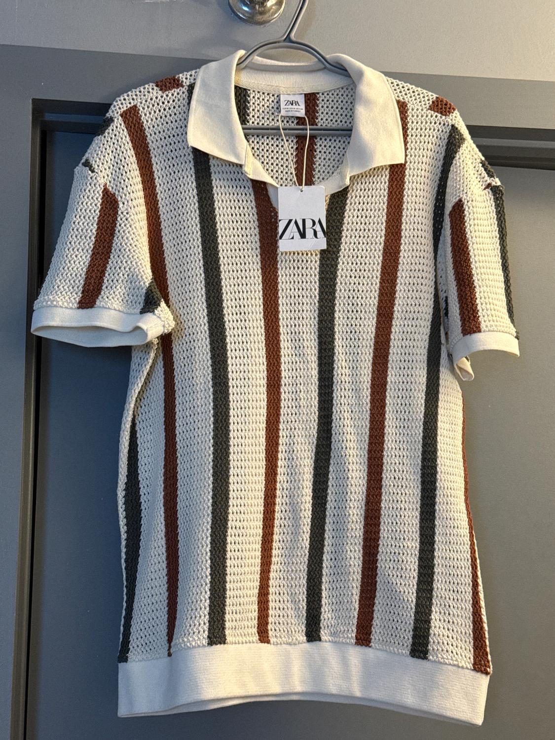 Knitted top with vertical brown and grey stripes, hanging on a hanger. Visible label with the text "ZARA".