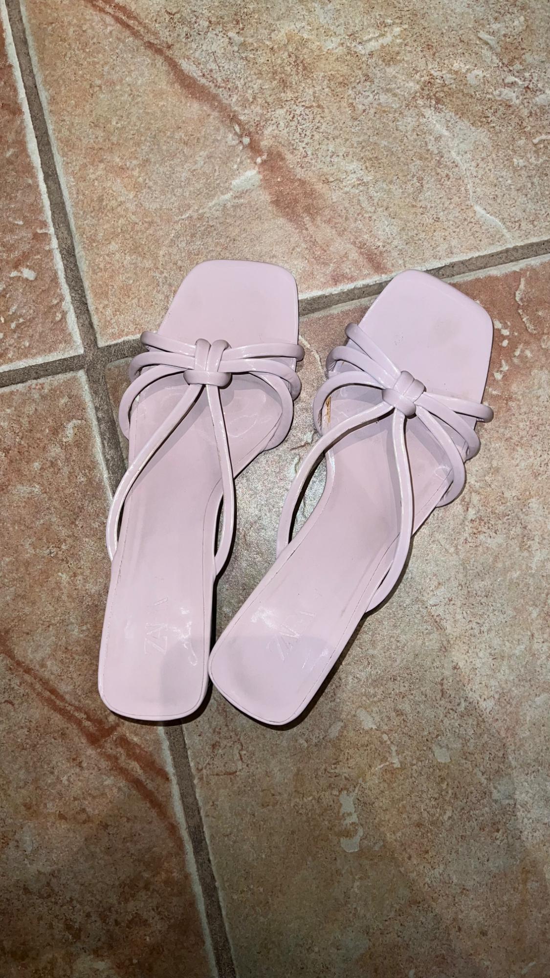 Lilac sandals with interwoven straps on a brown tiled floor. Square-toe design.