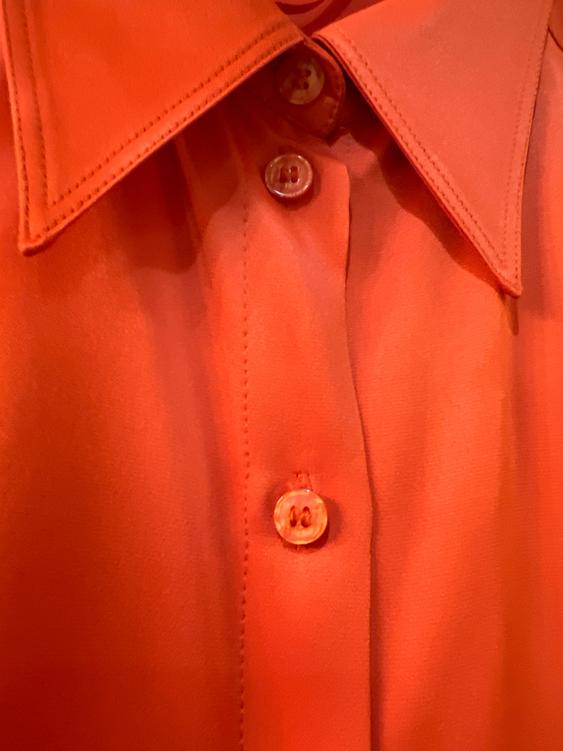 Orange shirt with a wide collar and visible buttons in the foreground. Soft fabric with detailed stitching.