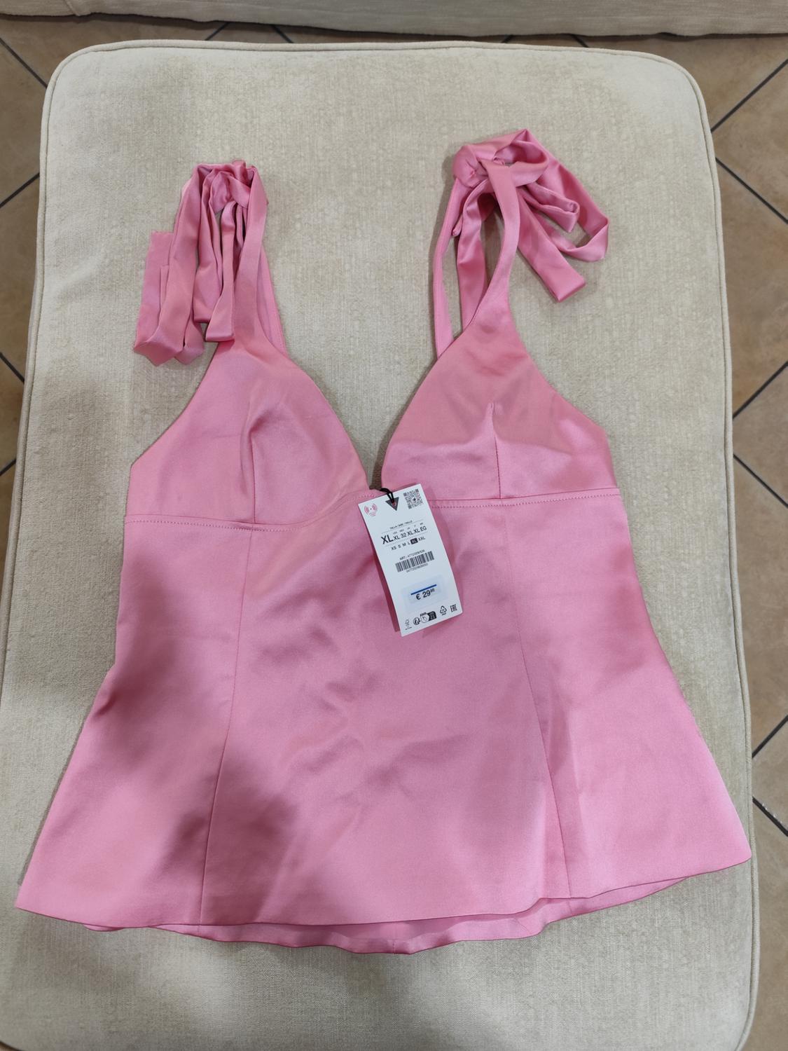 Pink top with wide straps and visible label, on a beige background. Soft and shiny fabric, elegant and feminine style.