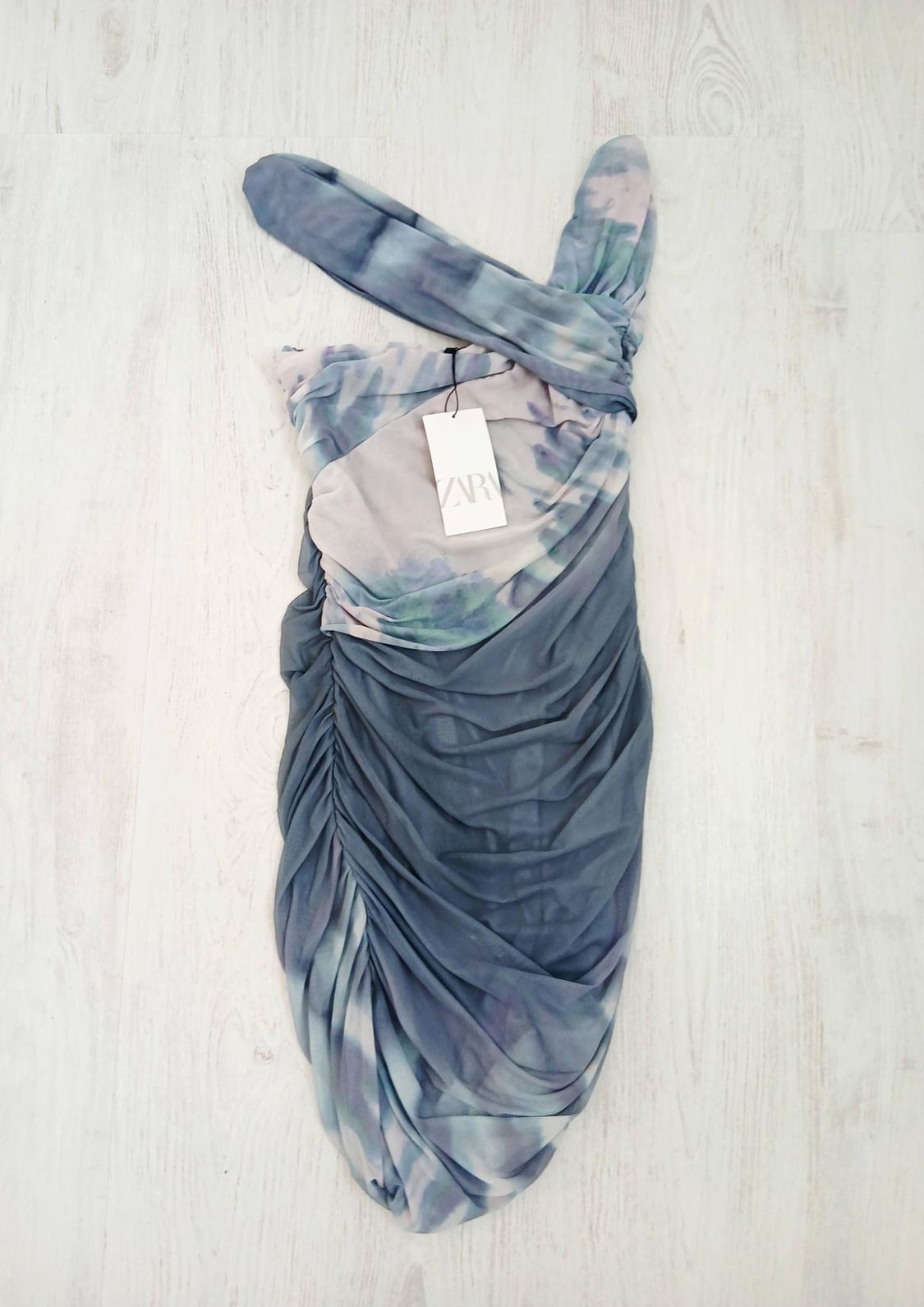 Draped dress in blue and lilac tones on a light background, with a Zara label hanging from the neckline.
