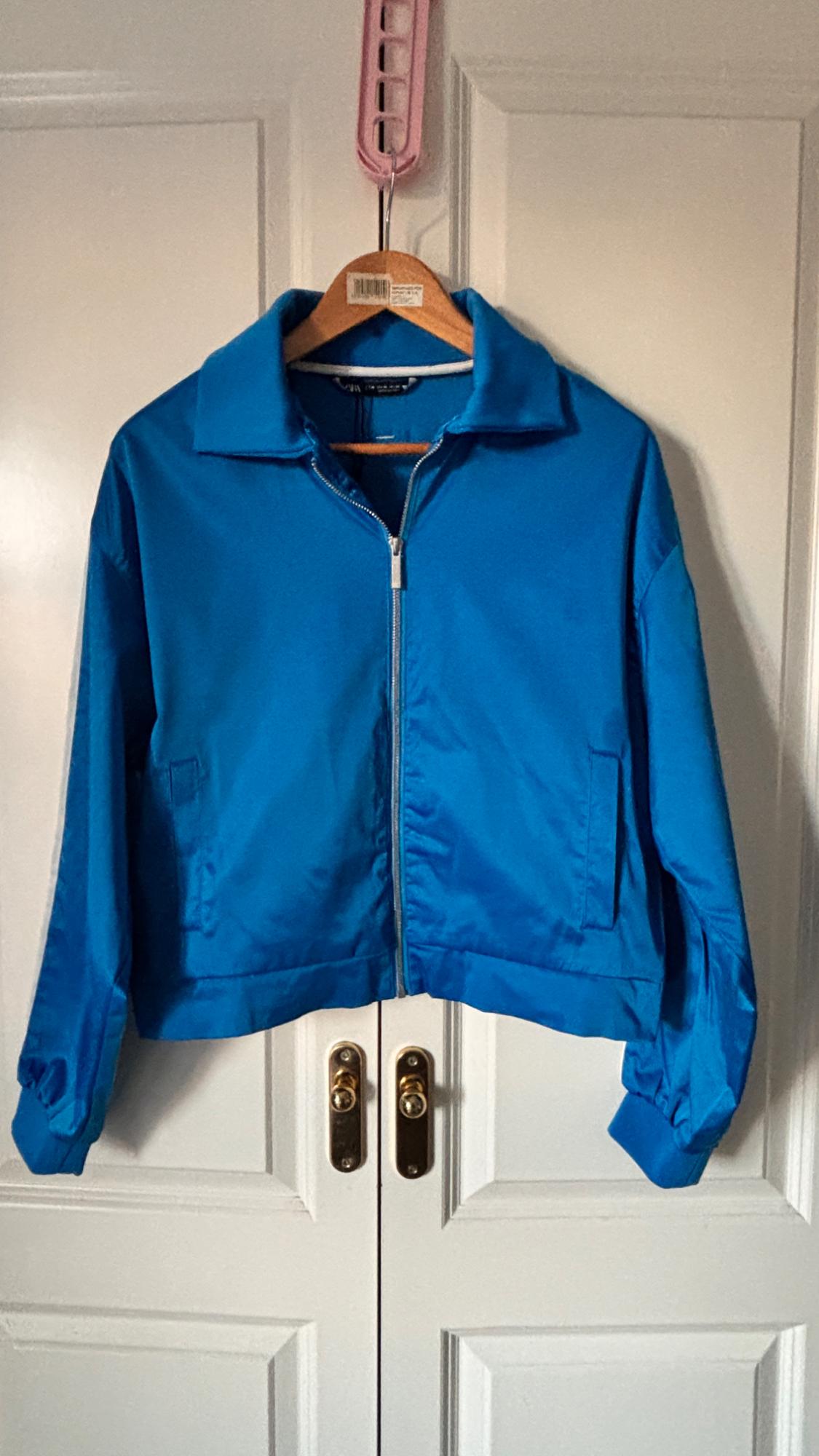 Blue zip-up jacket hanging on a wooden hanger in front of a white door with gold handles.