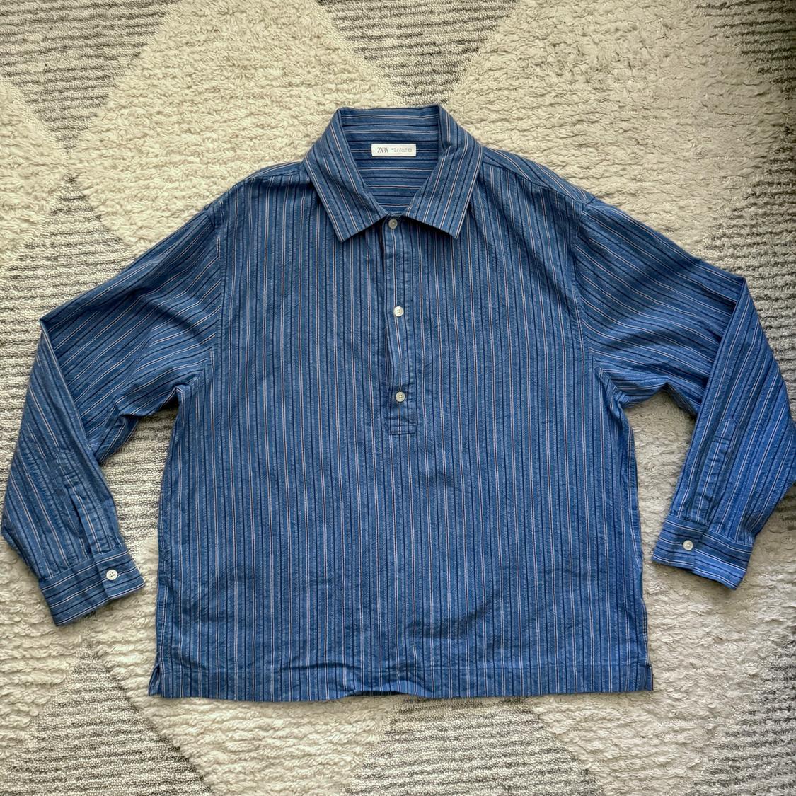 Blue striped shirt with collar and buttons, on a geometric pattern rug in gray and beige tones. Visible label: "ZARA".