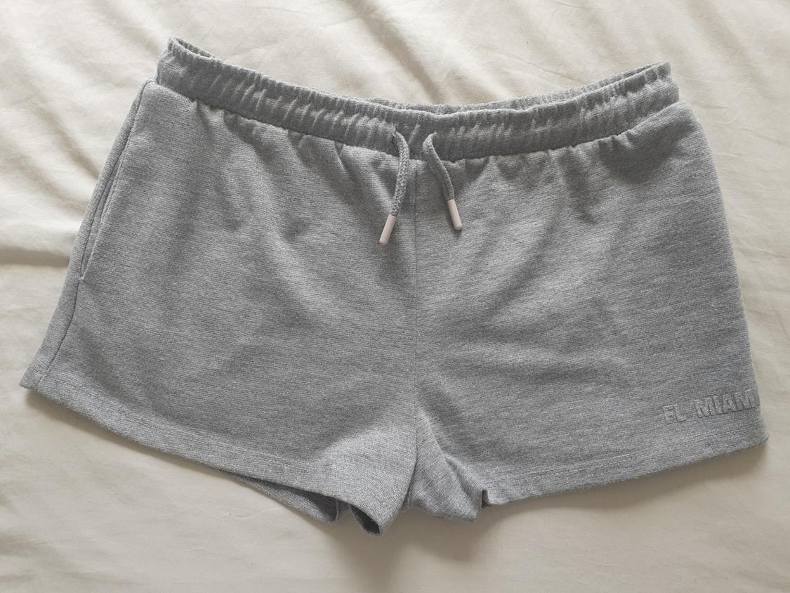Grey shorts with an elasticated waistband and drawstring on a light-coloured fabric. The text “FL MIAMI” is visible on the right leg.