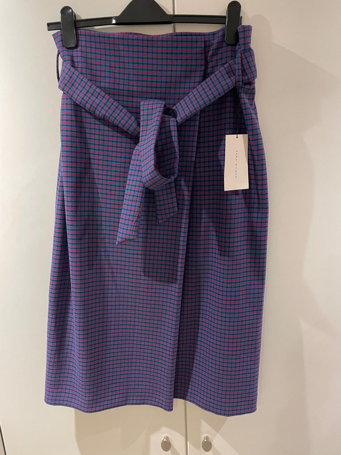 Front view of blue skirt with belt, small red check print, visible label hanging from the belt.
