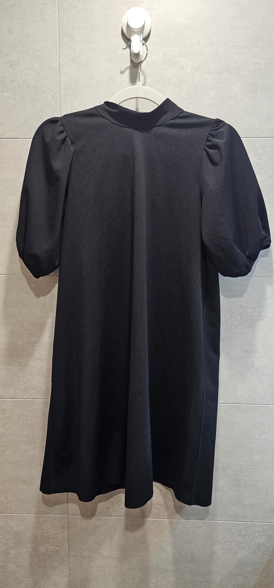 Black short puff-sleeved dress hanging on a white hanger against a grey tiled wall.