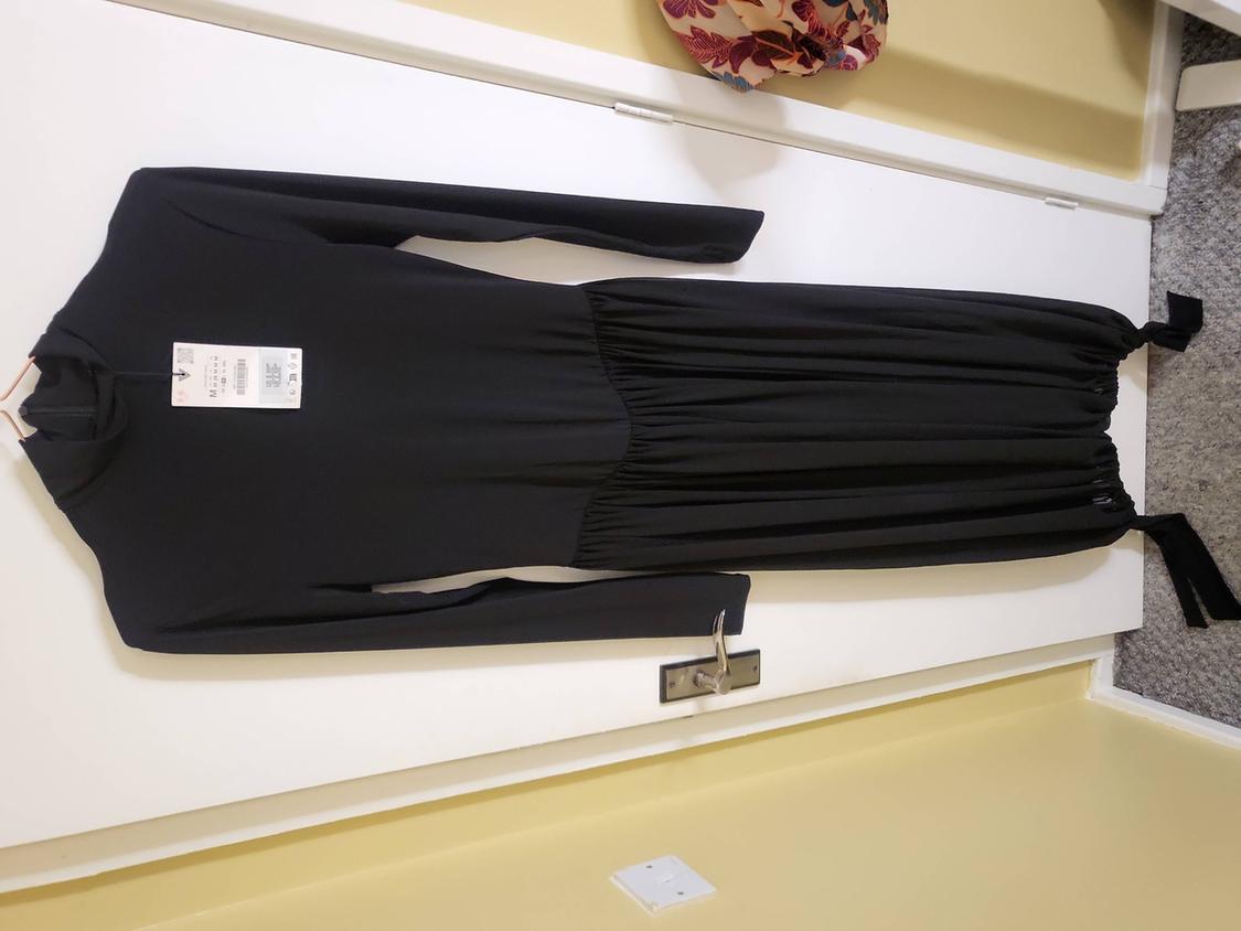 Black, long-sleeved dress hanging on a white door. Label visible on the collar. Yellow wall and grey carpet in the background.