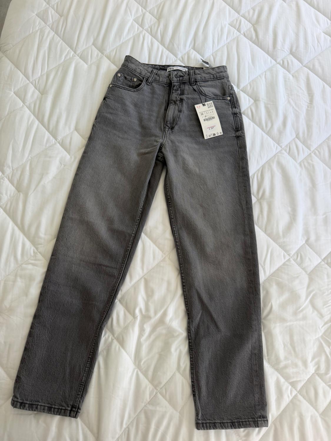 Grey denim jeans on a white quilted bedspread. Visible label with barcode and product details.