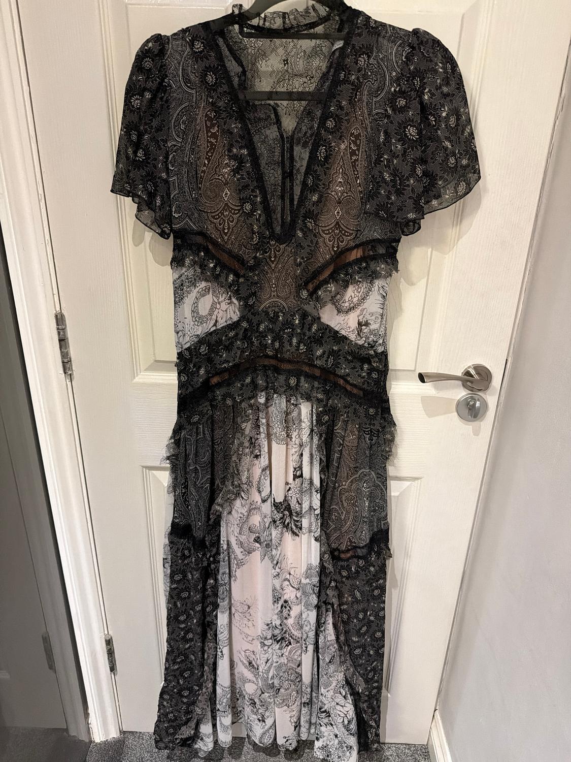 Long dress hanging on a door, with a paisley print in black and grey tones, short sleeves, and lace details.
