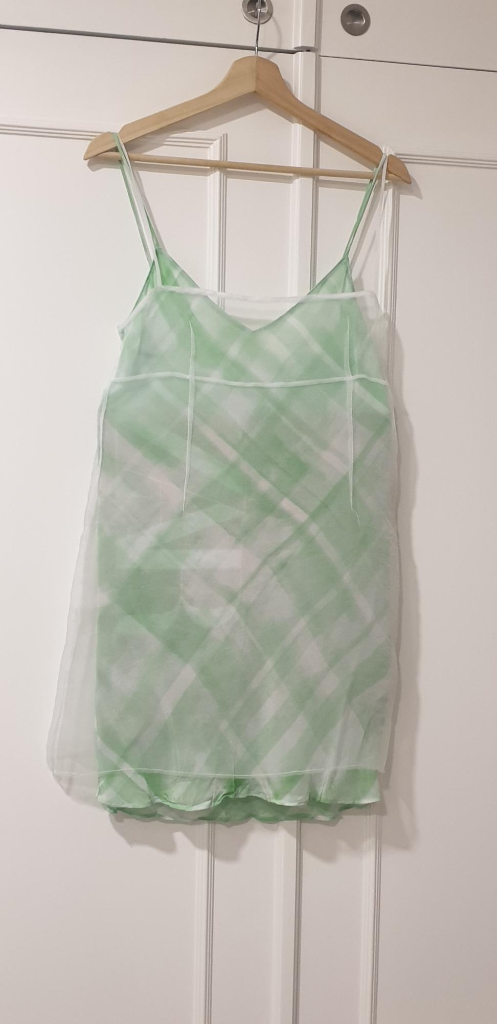Green strappy dress with white check print, hanging on a wooden hanger over a white door.