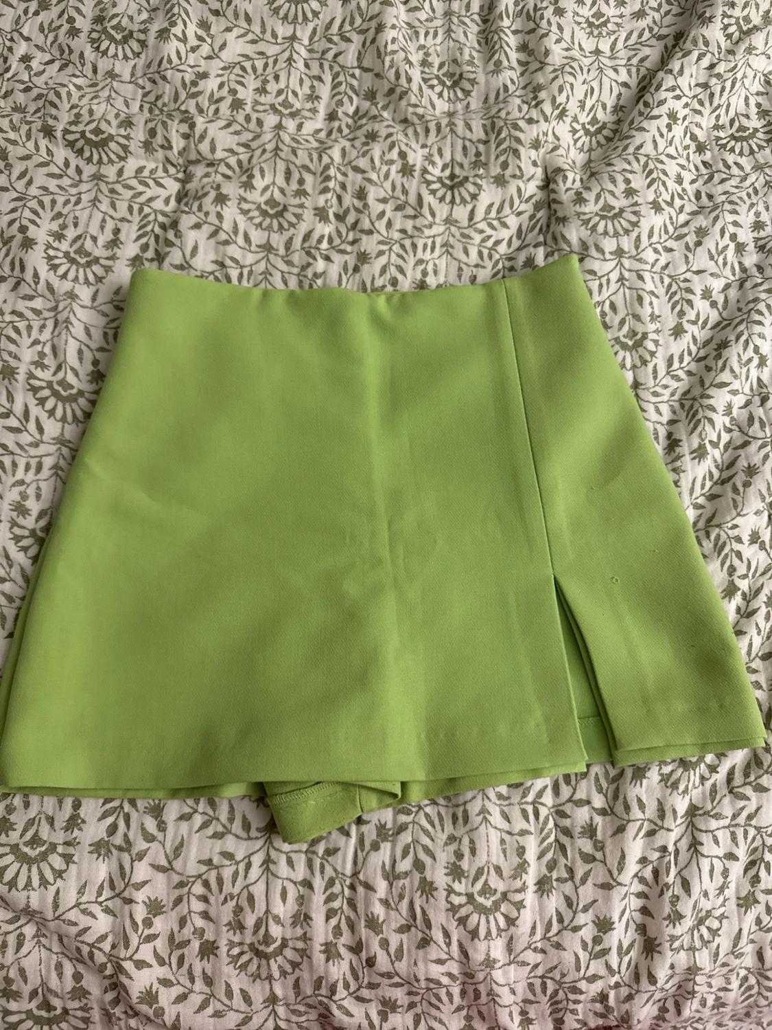 Light green culottes with a side slit, laid out on a textile surface with a leaf pattern.