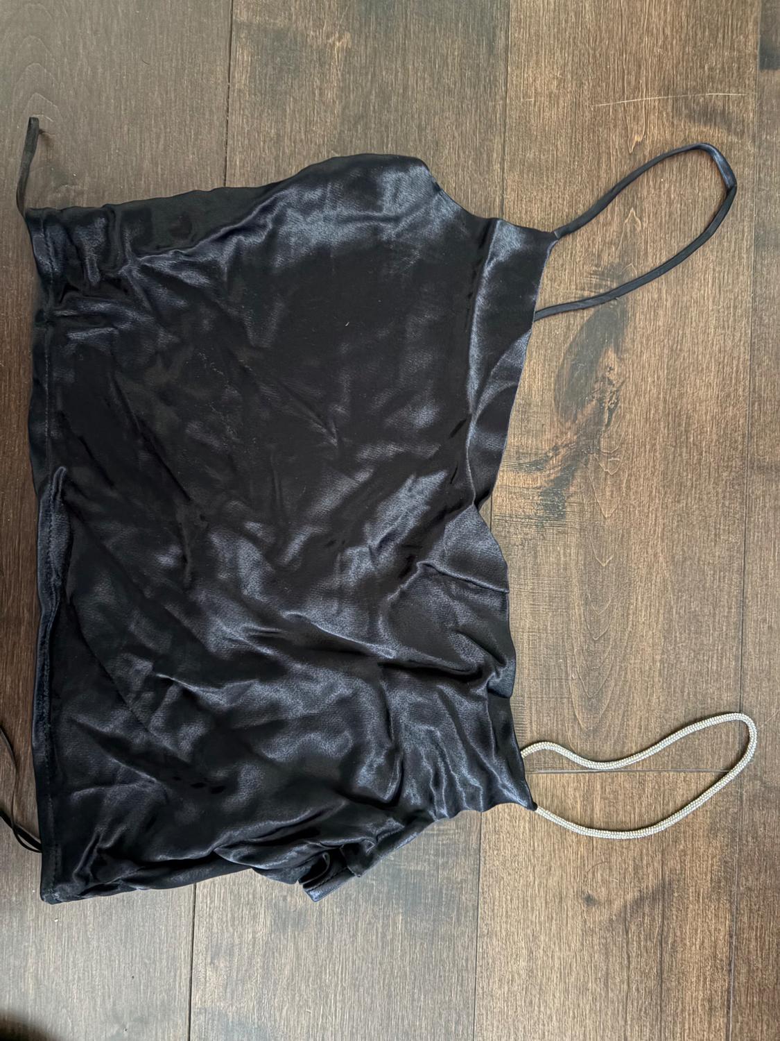 Shiny black crinkled top, with one thin strap and one silver diamante strap, laid out in a relaxed way on a wooden floor.