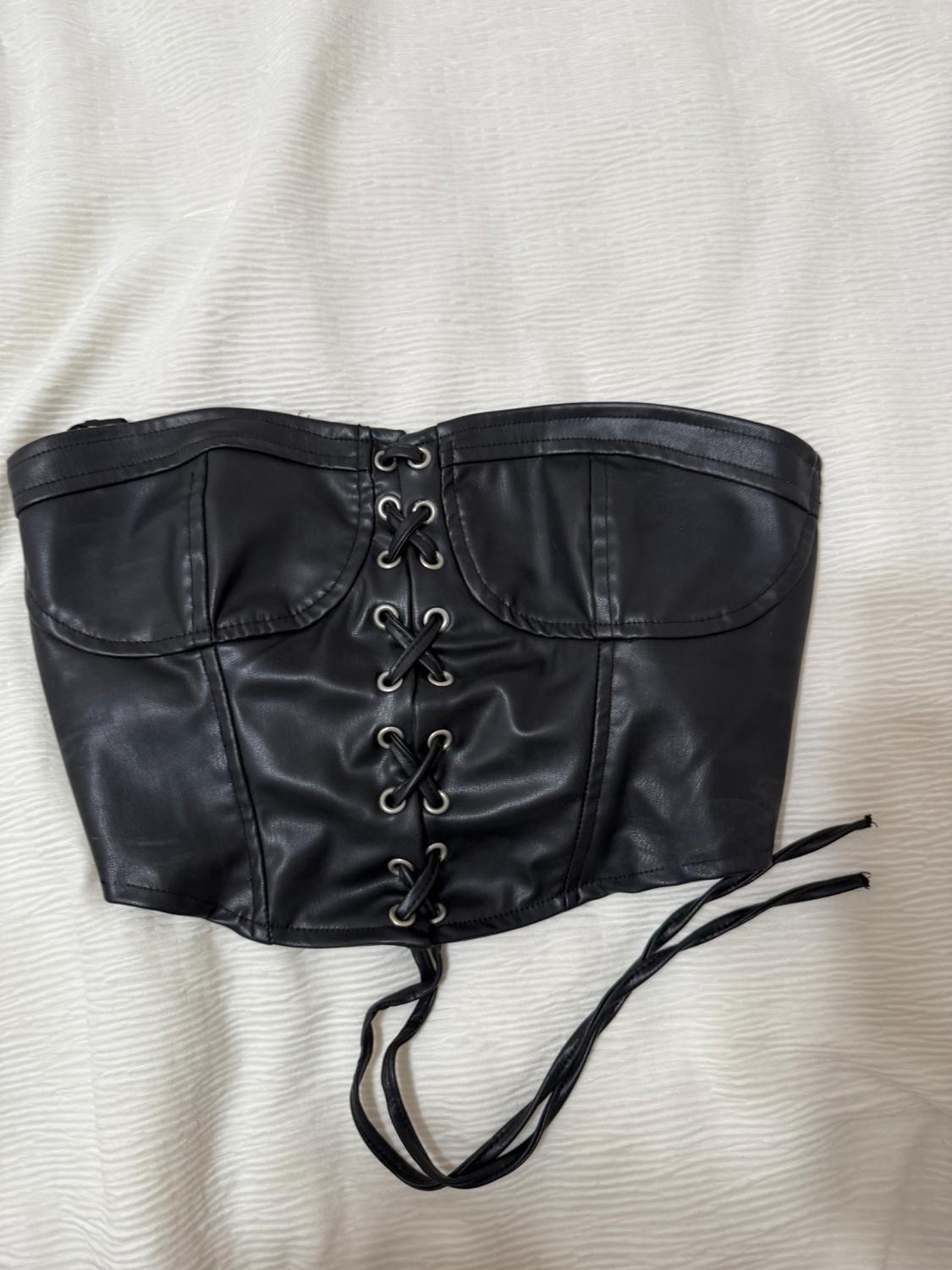 Black corset with criss-cross lacing at the front, on a textured white surface.