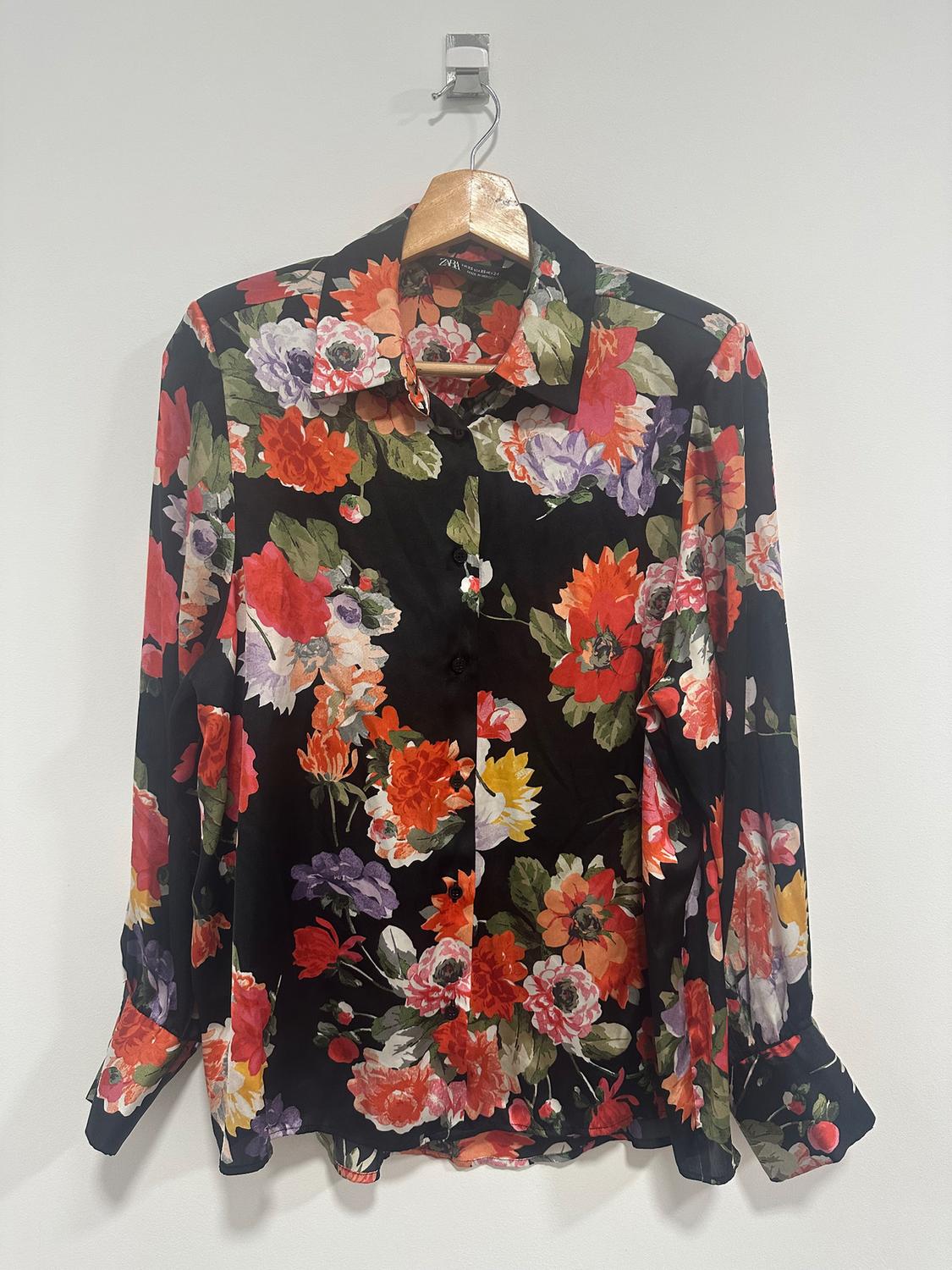 Black background shirt with a floral print in red, orange, purple, and green tones, hanging on a wooden hanger.