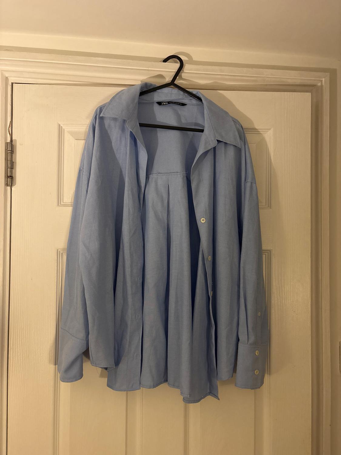 Light blue shirt hanging on a black hanger over a white door. The shirt has buttons and a classic collar.