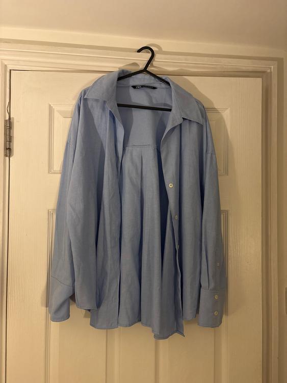 Light blue shirt hanging on a black hanger over a white door. The shirt has buttons and a classic collar.