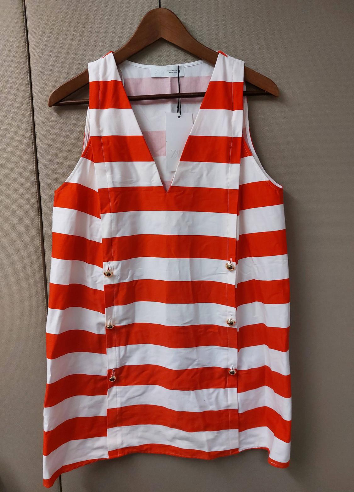 Sleeveless striped white and orange ZARA dress on a hanger. V-neck with six decorative gold buttons on the front.