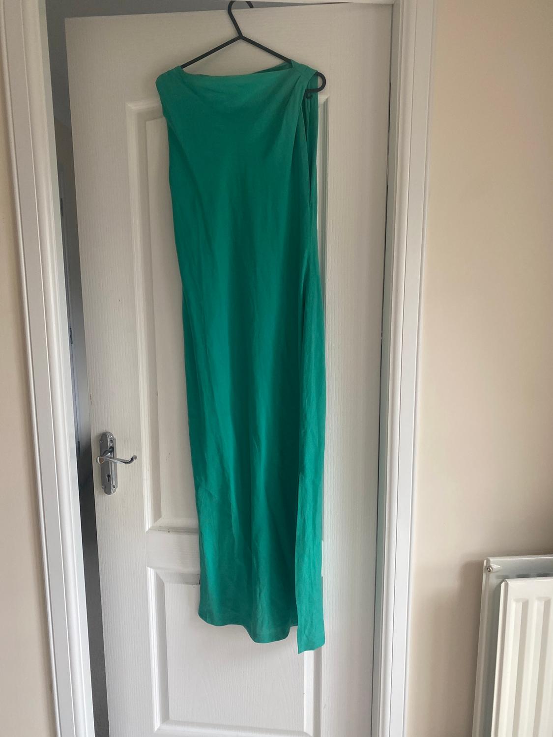 Long green dress hanging on a hanger over a white door. Indoor setting with natural light.