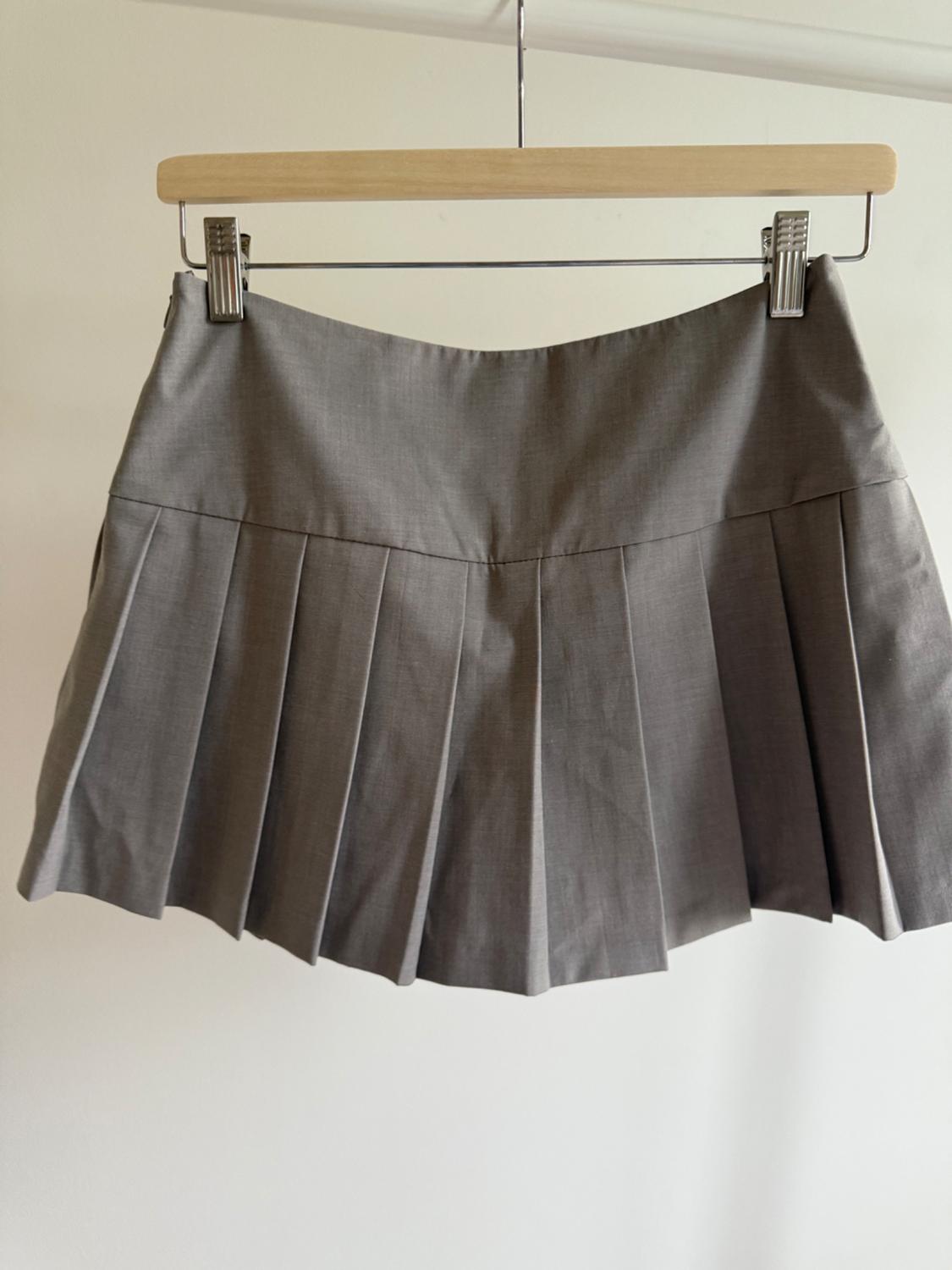 Short grey pleated skirt, hanging on a wooden and metal hanger against a white background.