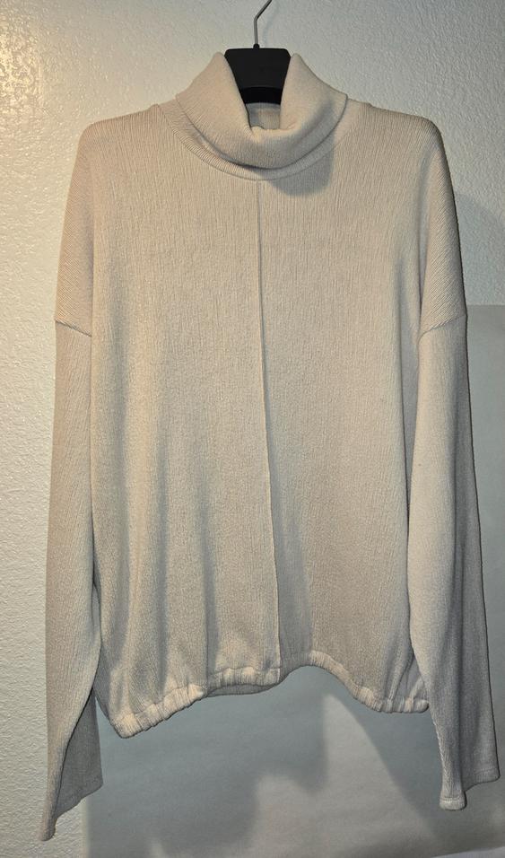 Beige turtleneck sweater hanging on a black hanger, with ribbed texture and white wall background.