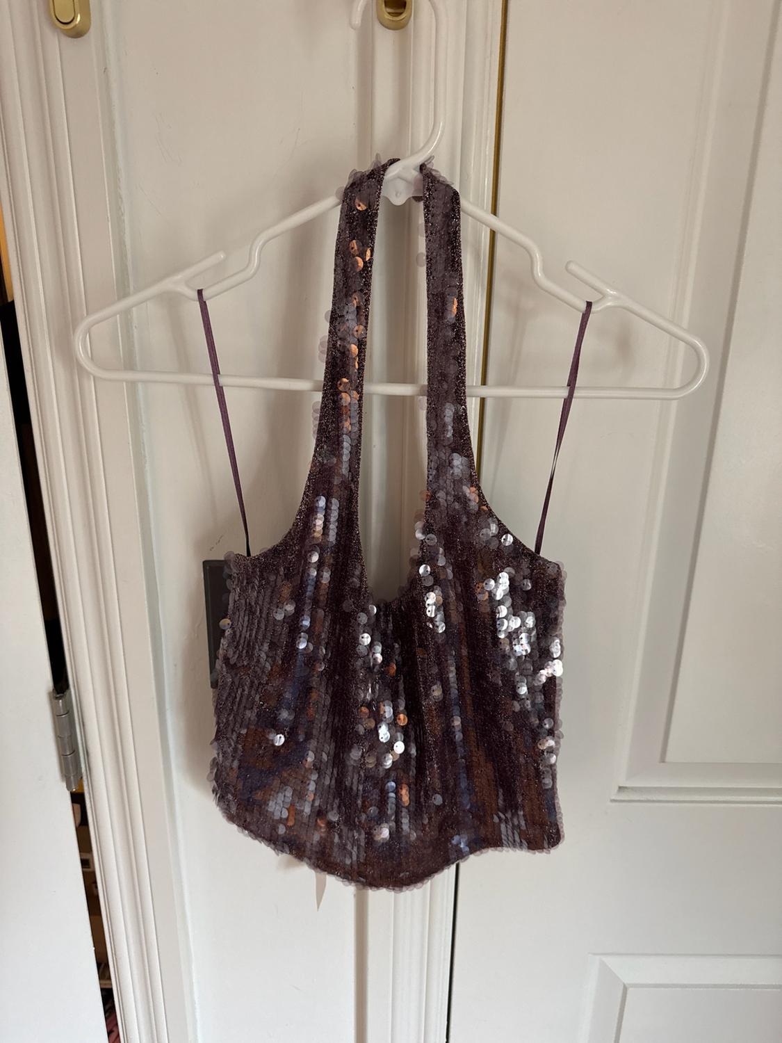 Sparkly sequin halter top hanging on a white hanger over a door.