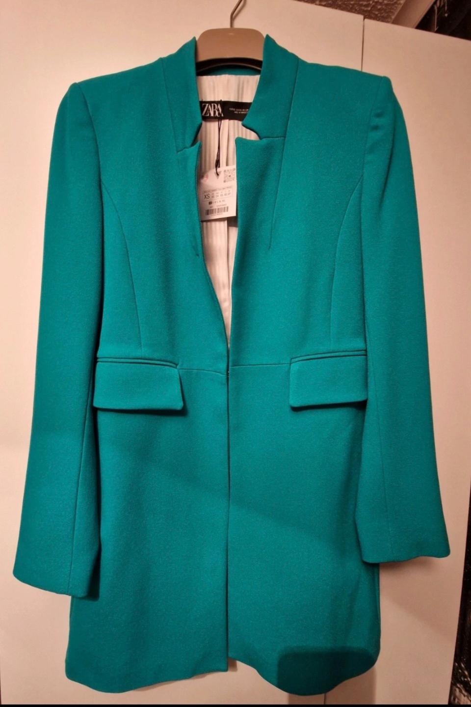 Turquoise jacket hanging on a hanger, with visible ZARA brand label and size XS. White background.