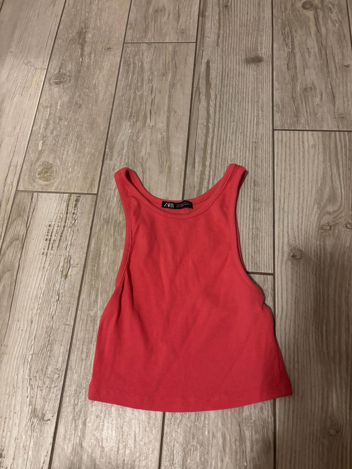 Pink ribbed camisole top on a light wooden floor. The label reads ZARA.